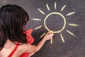 A little girl draws with colored chalk on the asphalt.
A drawing on a playground. A child draws a sun with chalk on an asphalt sidewalk.