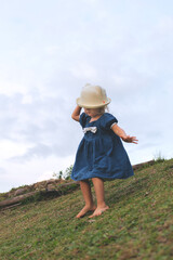 A little girl, in an adorable blue dress comes down the slide holding her panama from the wind