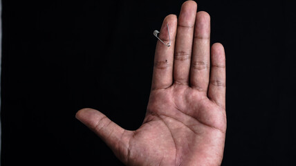 
The palm with the index finger is pierced by a pin, and has a black background