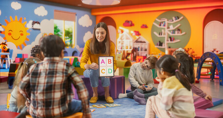 Happy Professional Kindergarten Teacher Using Tablet Computer to Show Numbers and Alphabet Characters to Smart Little Kids at a Modern Colorful Kindergarten. Female Educator Developing Social Skills