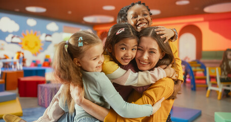 Boys and Girls Hugging Their Young Female Educator. Young Kindergarten Teacher and Cute Multiethnic Children Having Fun. Cheerful Kids are Happy to See Their Daycare Pedagogue