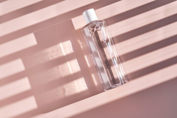 Bottle of facial toner or cleanser on a pink background with stripes shadows.