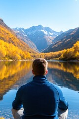 Fototapeta premium A tranquil scene features a person sitting by a serene lake, surrounded by vibrant autumn colors and majestic mountains, Perfect for wellness, nature, or motivational content,