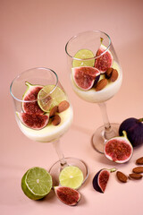 delicate dessert with figs and almonds in a glass on a high stem. Pink background.
