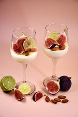 delicate dessert with figs and almonds in a glass on a high stem. Pink background.