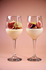 delicate dessert with figs and almonds in a glass on a high stem. Pink background.