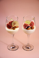 delicate dessert with figs and almonds in a glass on a high stem. Pink background.