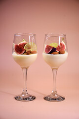 delicate dessert with figs and almonds in a glass on a high stem. Pink background.
