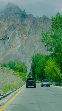 A black pickup truck drives along the Karakoram Highway with the jagged Passu Cones rising dramatically behind Passu village.