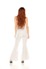 Obraz premium Fashion style rear view studio shott of beautiful young redhead woman. White wide leg pants and white sleevles shirt. Model standing and posing against white background