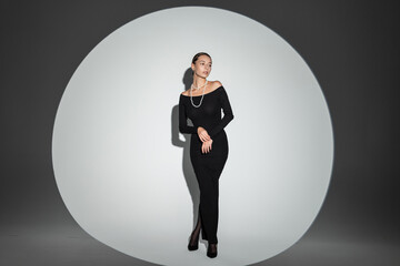 Charming glamorous chic woman in fashion long dress standing in studio. Pretty girl at party.