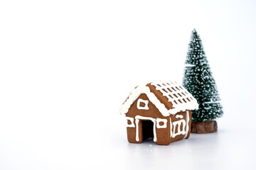 Merry Christmas Cookie Gingerbread House snow assembled and decorated with royal icing easy minimal style with a mini christmas tree on white background and copy space.