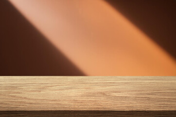 Empty wooden tabletop and a wall with beautiful shadows from the window in the background.