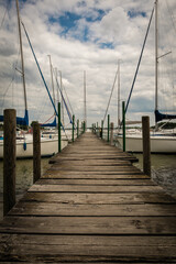 Obraz premium Wooden Dock Leading to Sailboats Under Cloudy Sky at a Serene Marina