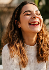 Fototapeta premium Joyful young woman with curly hair laughing outdoors in warm sweater