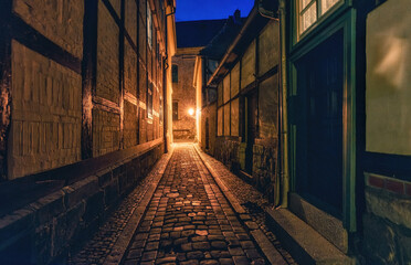 Schmale schwach beleuchtete Gasse zwischen Fachwerkhäuser bei Nacht in Quedlinburg.