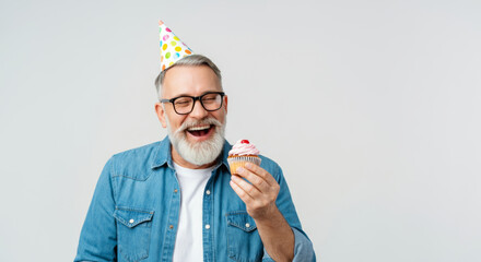 Joyful elderly man celebrating with birthday cupcake and party hat