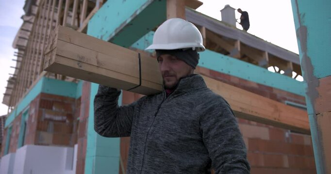 Carpenters carrying long wooden beams at construction site, teamwork in house building project, two workers in hard hats and gloves, residential construction, building materials