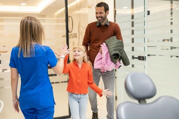 Obraz premium A cheerful young girl high-fives a smiling dentist in a modern dental office, celebrating a successful dental visit with her parent looking on happily.