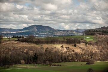 Fototapeta premium Bergkette der schwäbischen Alb mit Grünfläche in Flusstal mit Hang und Bäumen und Lichtfleck von Sonne und Wolkenhimmel