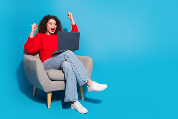 Full size photo of pretty young girl sit armchair netbook winning celebrate wear trendy red outfit isolated on blue color background