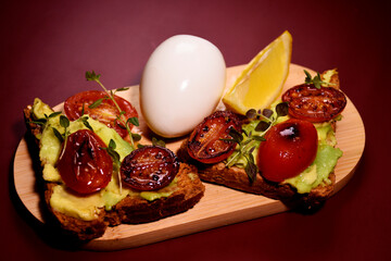 Healthy breakfast. toast with avocado paste and fried tomatoes, boiled egg on a wooden board.