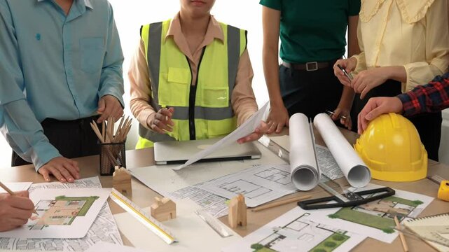 Smart architect and safety engineer discussion about building blueprint on table with architectural document, measurement tools and wooden block scatter around at modern office. Closeup. Delineation.