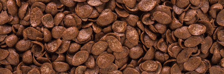 Dark brown dry chocolate cereal flakes background. Closeup. Wide banner. Top down view.