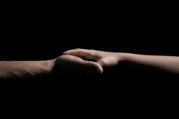 Holding hands over a black background a child and adult hold hands
