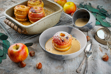 Traditional oven baked apples with crushed nuts, cinnamon and butter served with homemade vanilla sauce as close-up in a design plate