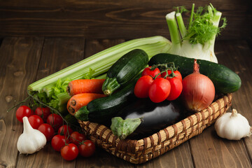 A wicker basket filled with fresh vegetables on wooden rustic table. Still life.