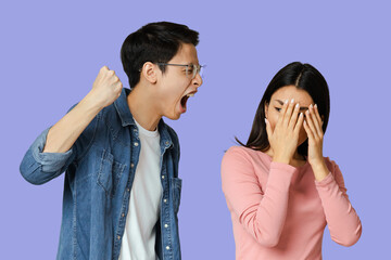 Domestic violence. Young asian man threatening his girlfriend with his fist, gray studio background