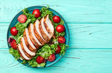 Grilled chicken breast ( fillet ) with lattuce salad and cherry tomatoes . Top view
