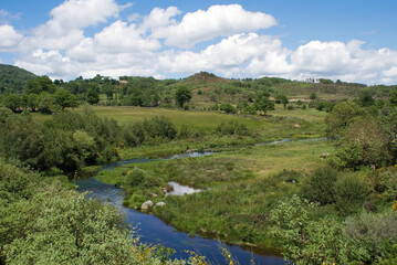 Rio a serpentear vegetação verde, com um céu com nuvens bem defenidas. Este rio é o Rio Cávado em Portugal.