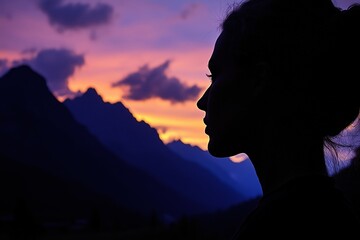 Woman's profile against a mountain sunset, dramatic silhouette and colorful dusk sky.