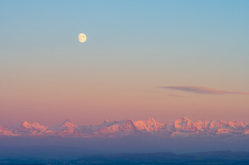Fototapeta premium Beautiful panorama of the Swiss Alps at sunset with the moon in the sky in the background
