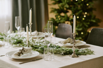 Medium close up of festive table decorated with polished champagne glasses and white plates, center of table decorated with amazing pine garland