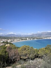 Obraz premium An expansive view of a coastal town nestled between lush green hills and the stunning blue Mediterranean Sea. Captures the tranquility and beauty of this scenic landscape.