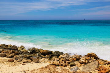 Rocky shore with turquoise waves gently splashing on bright sunny day on Caribbean island of Aruba.