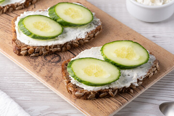 Slices of whole grain bread topped with cream cheese and fresh cucumber arranged beautifully at a rustic wooden table
