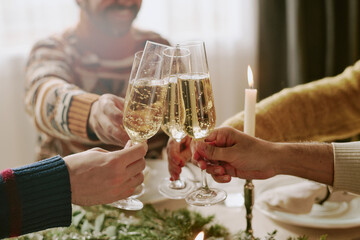 Unrecognizable group of friends clinking polished crystal glasses with sparkling wine while partying together