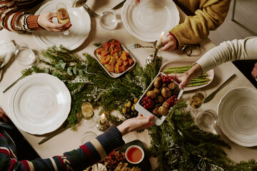 Top down shot of unrecognizable friends at decorated table drinking sparkling wine and eating traditional food for Christmas © AnnaStills