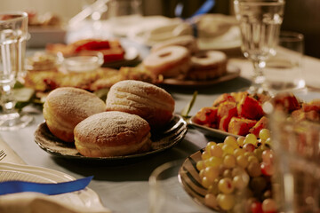 Medium close up of fresh baked donuts covered with powdered sugar surrounded with other pastries and appetizers on festive table