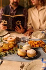 Vertical shot of table with huge number of fresh baked pastry and unrecognizable couple reading Torah