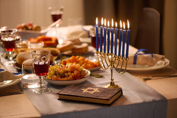 Medium close up of lit blue candles next to Torah on table with huge number of traditional treats and alcoholic beverages