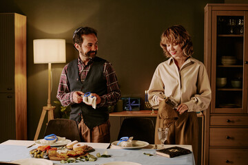 Biracial couple standing next to table and polishing wine glasses while preparing for Hanukkah celebration at home