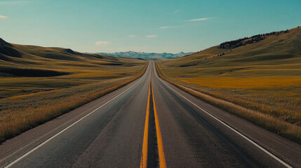 Fototapeta premium Endless road through green fields and mountains on a clear sunny day