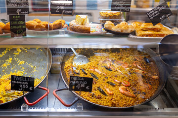 Fresh Paella and different Spanish food, goods on a street food market. Huge pots with various types of paella on a counter at the central market