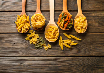 Colorful pasta varieties displayed in wooden spoons arranged on a rustic wooden surface for culinary inspiration and food photography