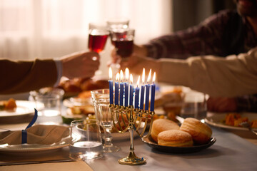 Medium close up of lit blue candles in golden candlestick on festive table, unrecognizable friends clinking glasses with red wine in blurred background